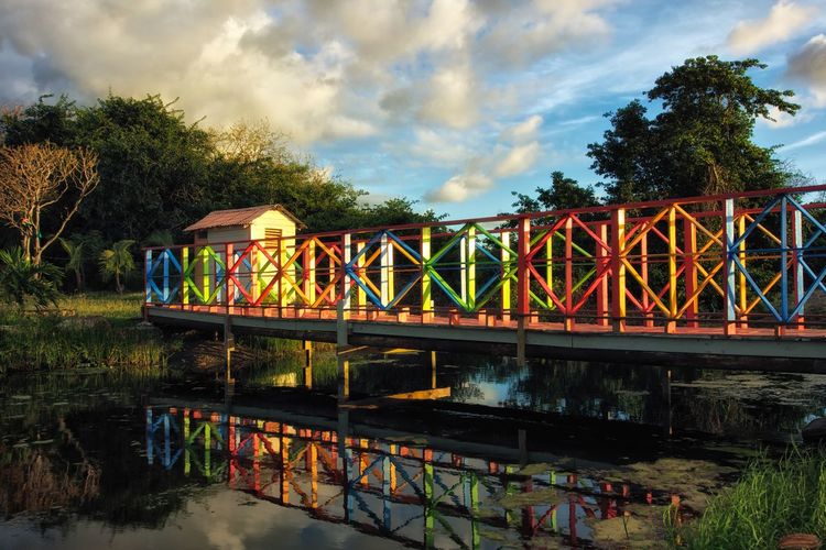Multi colored bridge over river against cloudy sky