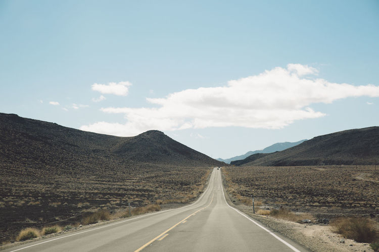 Empty road leading towards death valley mountains against sky