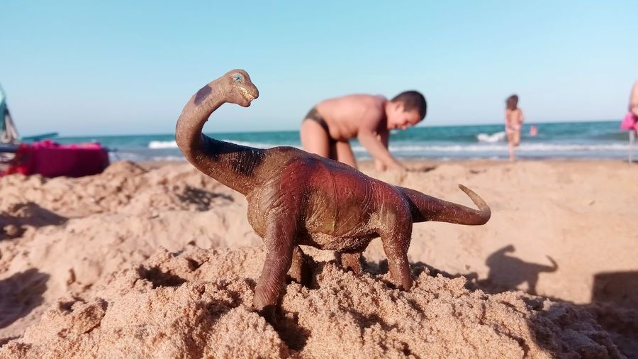 Toy dinosaur at beach against clear sky