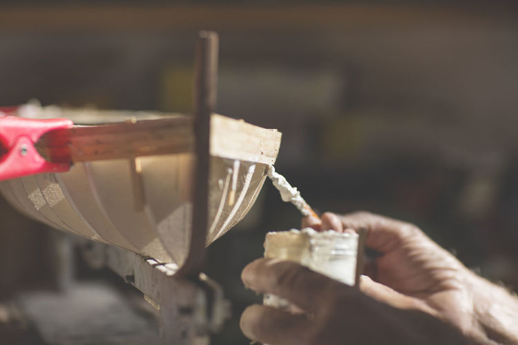 Cropped hands of man making wooden model boat at workshop