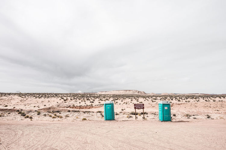 Rare view of portable toilets in front of a dune on beach against sky