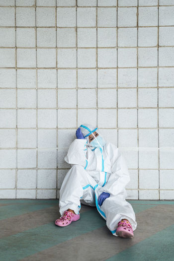 Contemplating female nurse with head in hands sitting against tiled wall