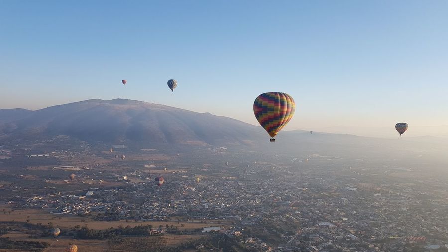 Hot air balloons flying over landscape against clear sky