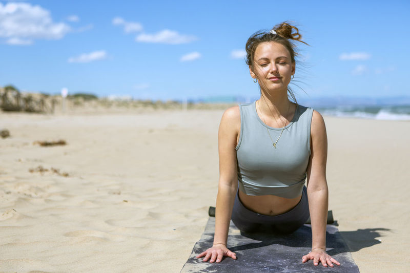 Woman doing pilates on the shore of the beach in sportswear