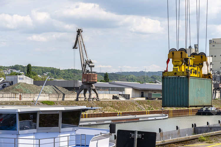 A container gantry crane on a rail loads the container into a barge standing on the banks of  river
