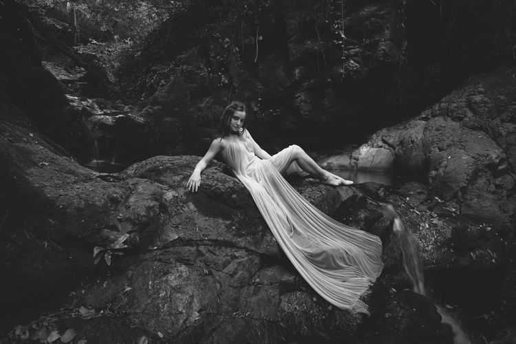 Portrait of young model wearing dress while sitting at waterfall
