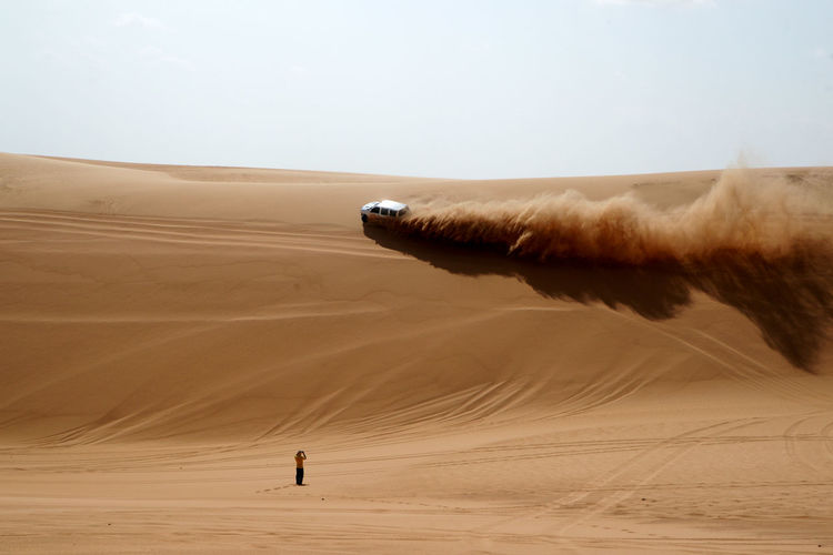 Rear view of man standing near off-road vehicle on desert
