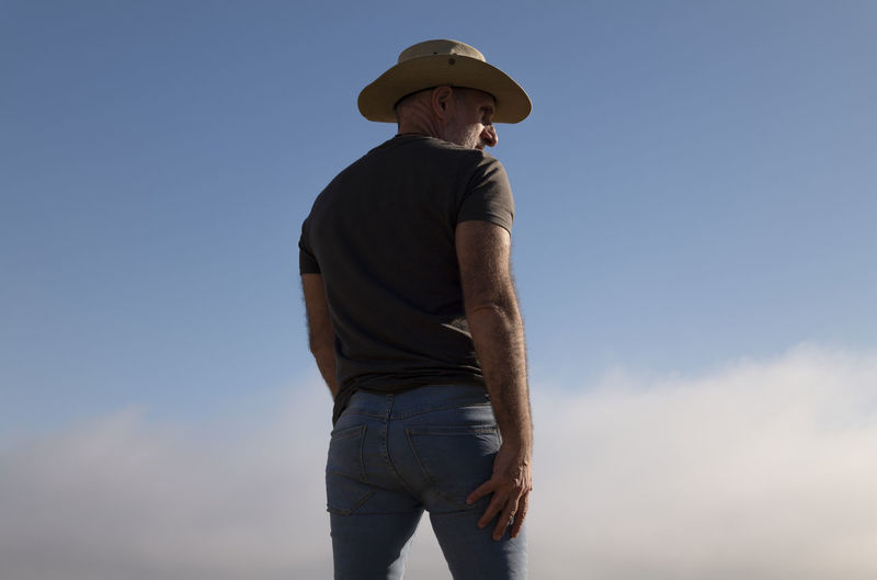 Rear view of adult man in cowboy hat and jeans against blue sky