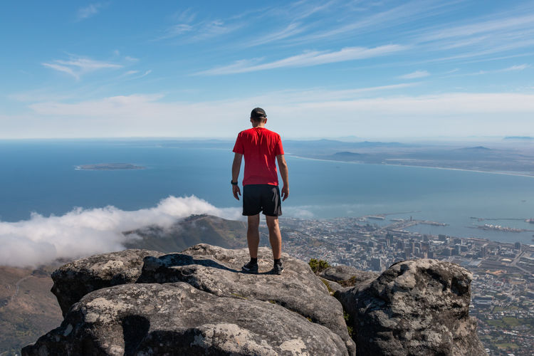 Man in red shirt looking down to cape town, south africa from top of table mountain