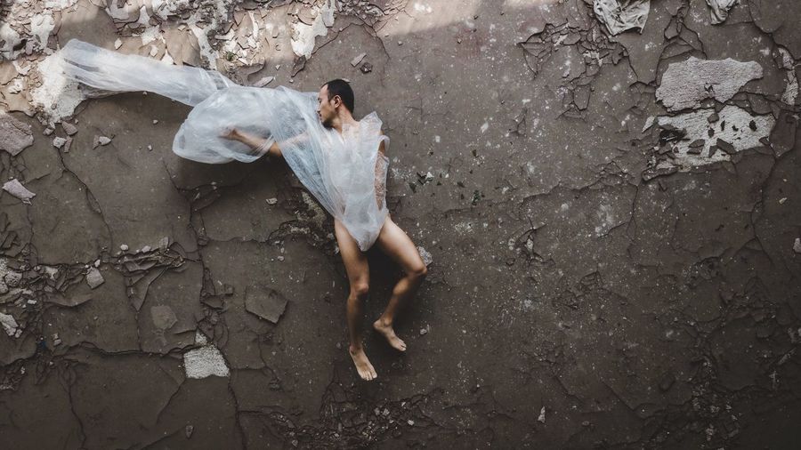 High angle view of naked man wrapped in plastic lying on abandoned floor