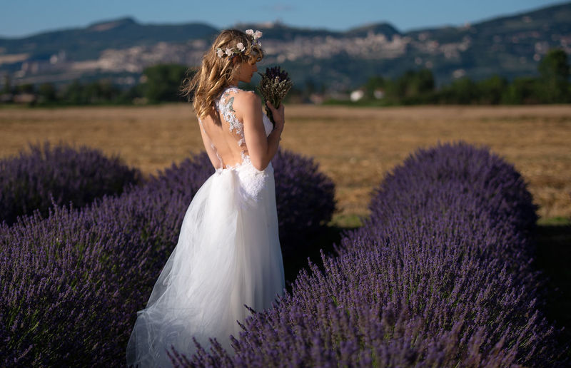 Bride holding flowers while standing amidst plants on field