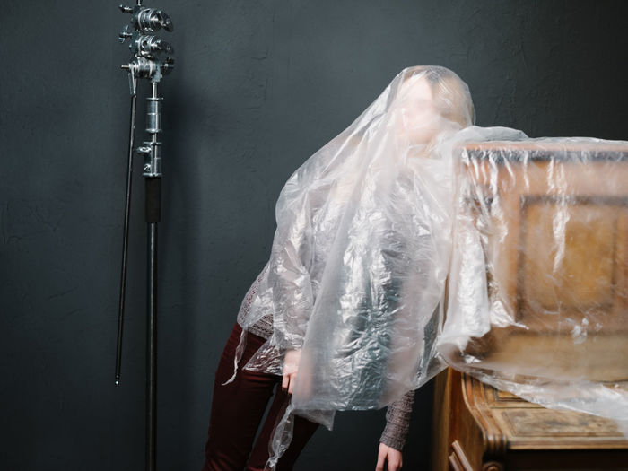 Woman wrapped in plastic standing by grand piano