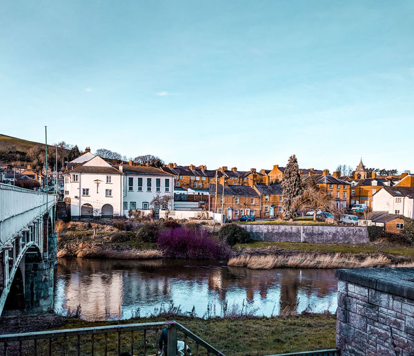 Bridge over river by buildings against blue sky