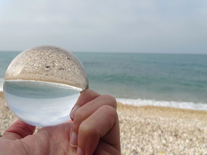Cropped hand holding crystal ball at beach