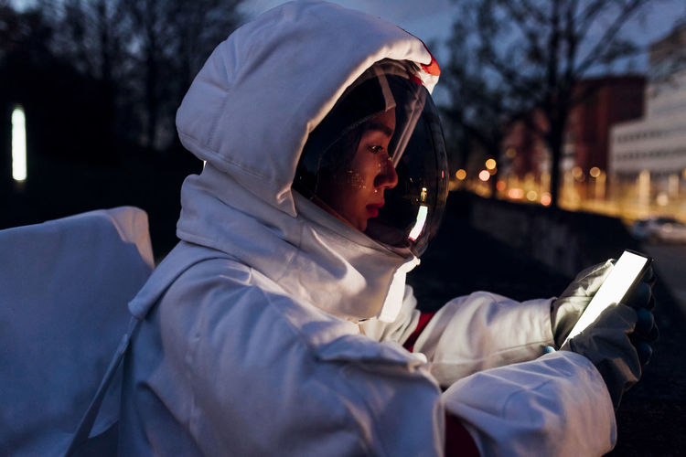 Young female astronaut using mobile phone at night