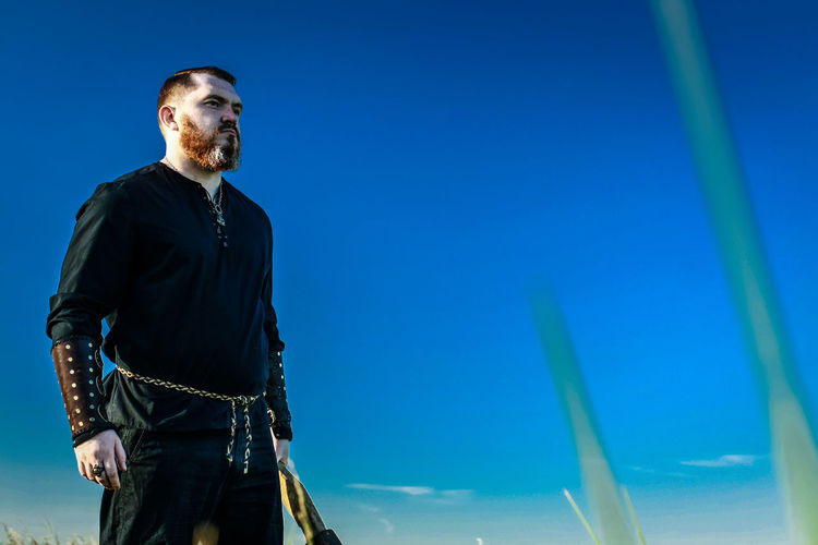 Low angle view of man in viking costume against clear blue sky