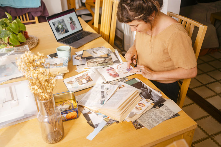 Graphic designer sticking paper clippings in book working at home