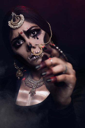 Close-up of young woman in traditional clothing with spooky make-up against black background