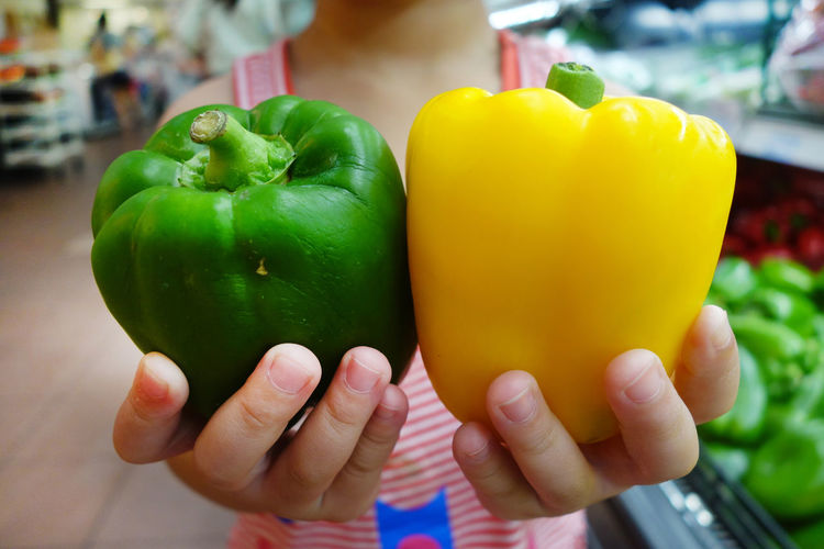Midsection of child holding bell peppers in store