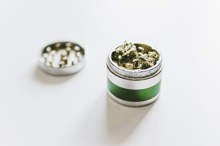 Close-up of marijuana in metallic grinder on white table