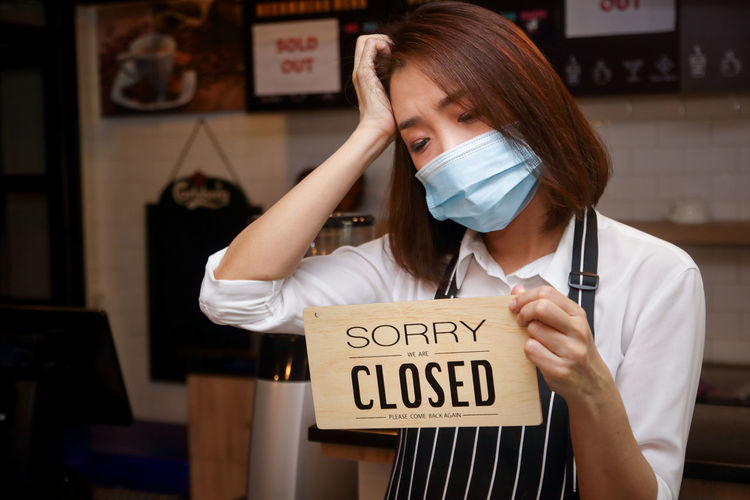 Woman wearing mask holding closed sign at cafe