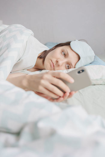 Woman using smart phone by lying on bed home