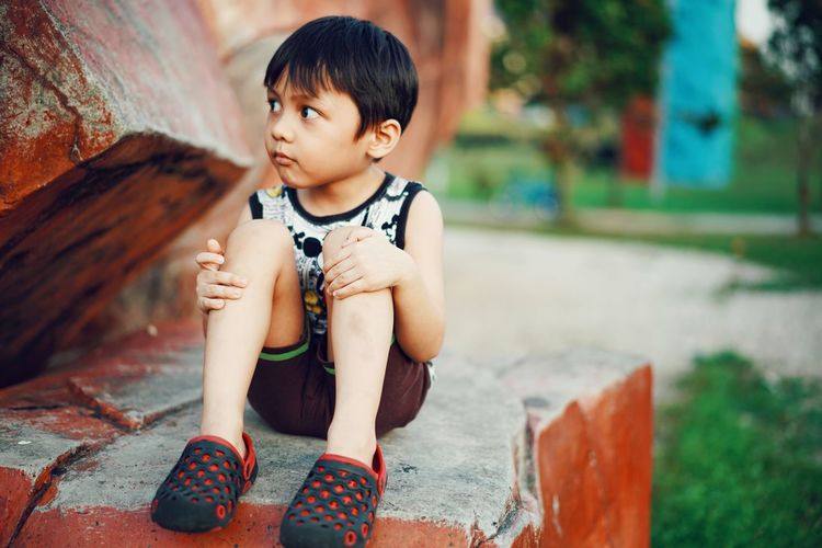 Cute boy looking away while sitting on wall