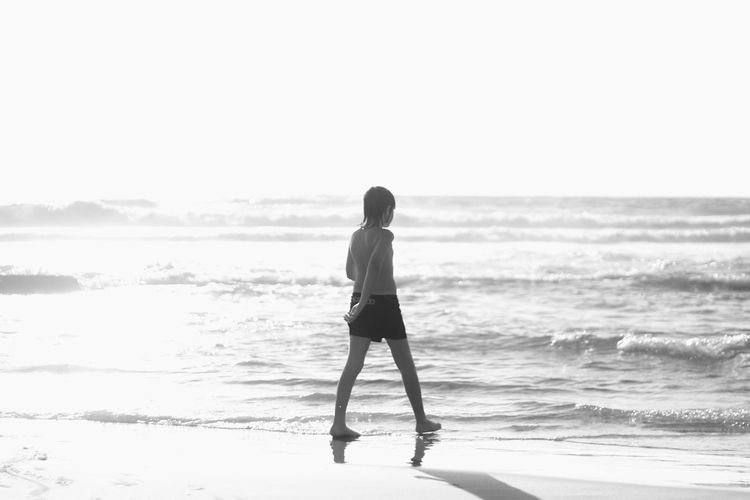 Full length of shirtless boy walking at sea shore against clear sky