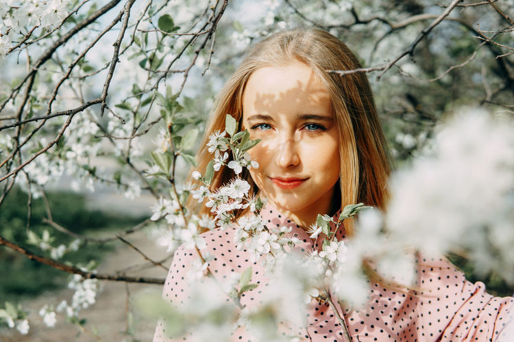 Blonde girl on a spring walk in the garden with cherry blossoms. female portrait, close-up. 