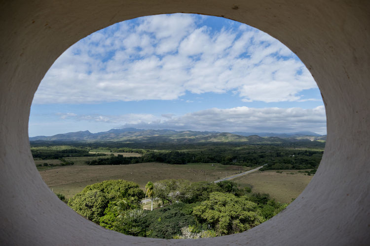 Scenic view of landscape against cloudy sky seen from circle window