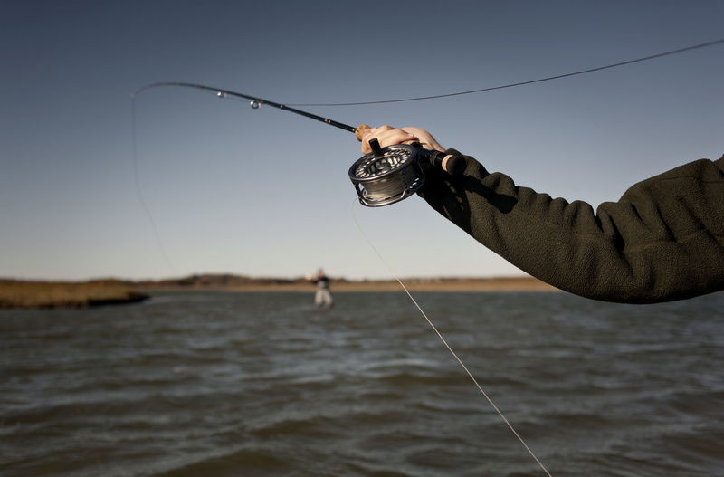 Cropped image of man holding fishing rod against clear sky