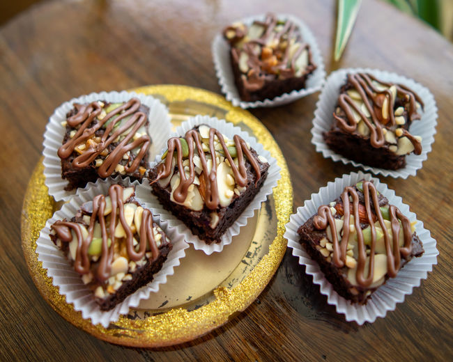 Chocolate brownie cubes with chocolate drizzle in paper cups on a wooden background.