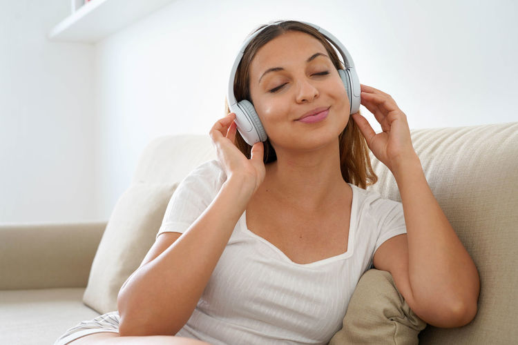 Beautiful young woman wearing headphones sitting on sofa