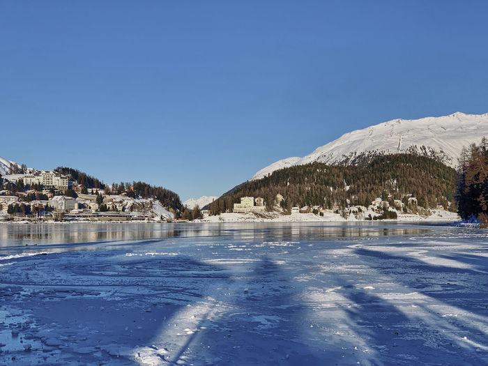 Scenic view of frozen lake by snowcapped mountains against clear blue sky
