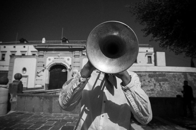 Musician playing trumpet while standing against building