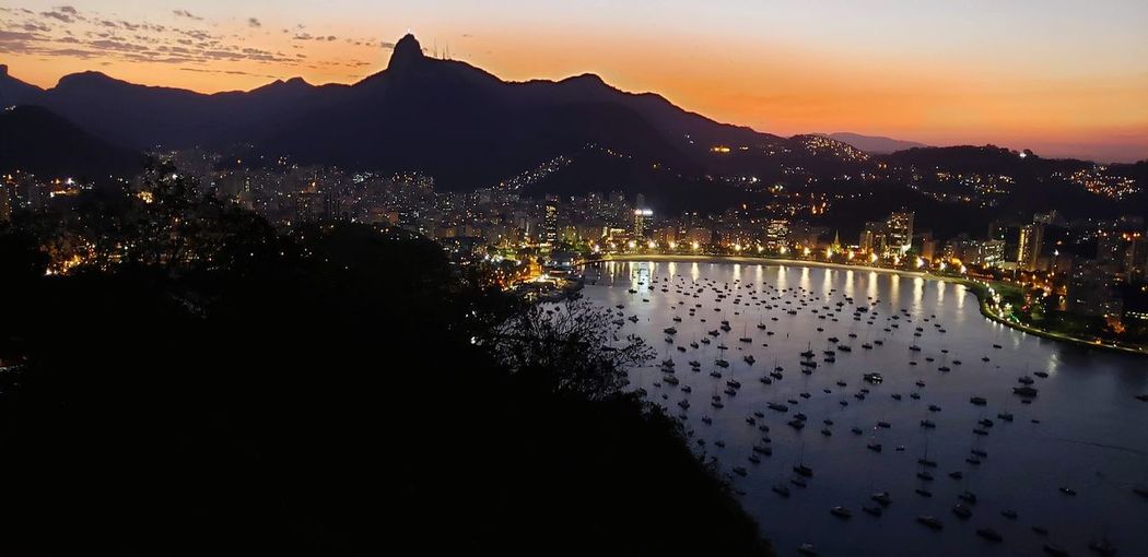 Scenic view of lake by illuminated city against sky at sunset