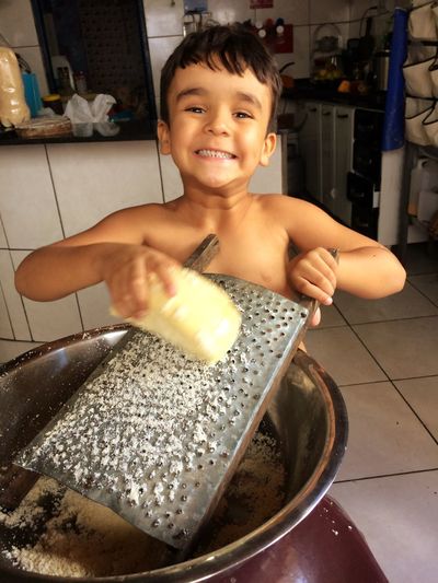 Portrait of smiling boy grating cheese in container