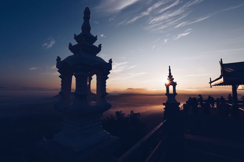 Sculptures over railing at observation point against sky during sunset