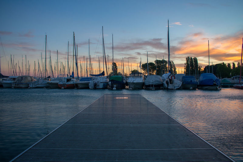 Sailboats moored at harbor against sky during sunset