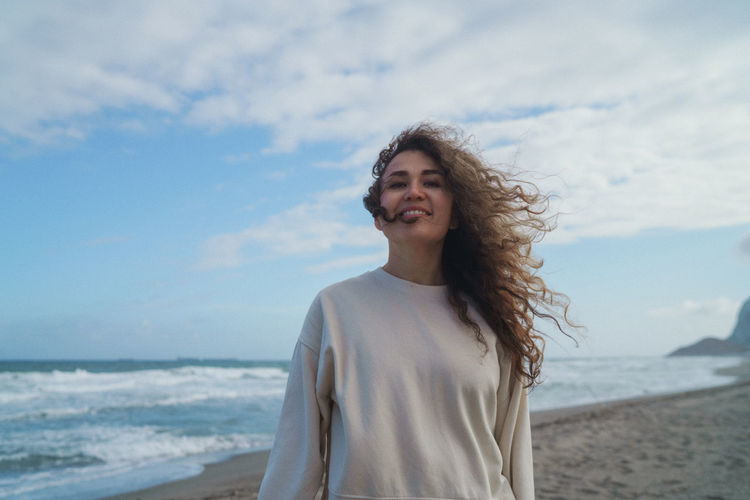 Happy young woman standing on beach against sky
