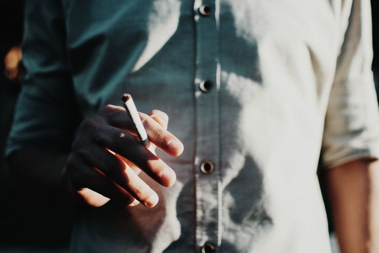 Midsection of man holding cigarette 