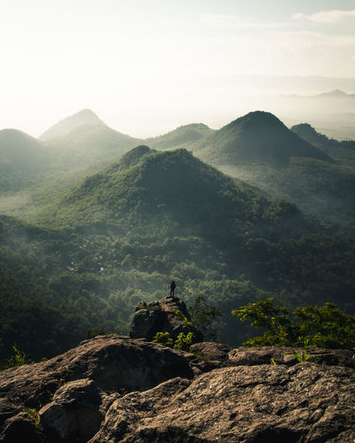 Scenic view of mountains with man standing on rock against sky