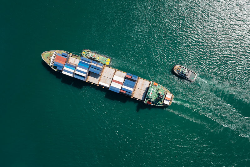 Aerial top view container ship and tugboat dragging floating in green sea, business and industry 