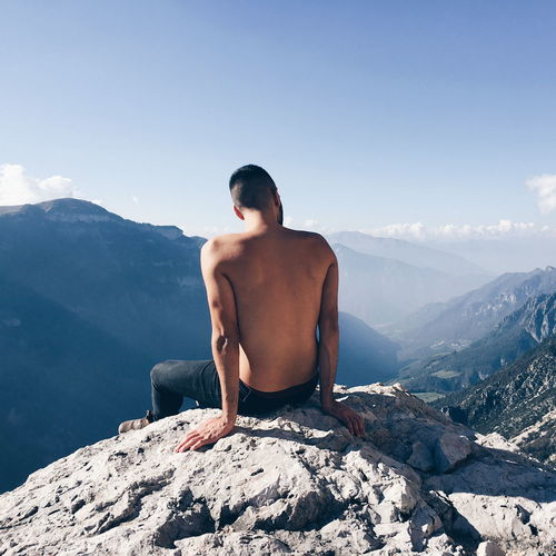 Rear view of shirtless man looking at mountains against sky
