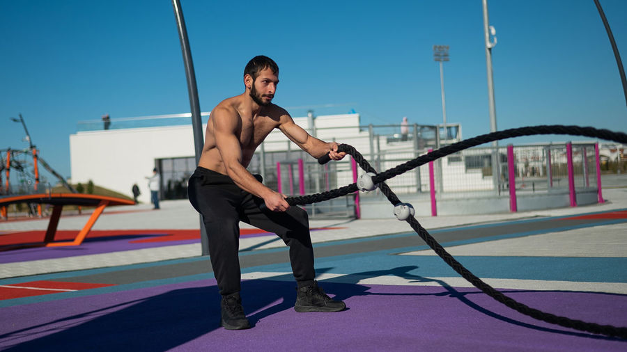 Full length of shirtless man exercising battle rope