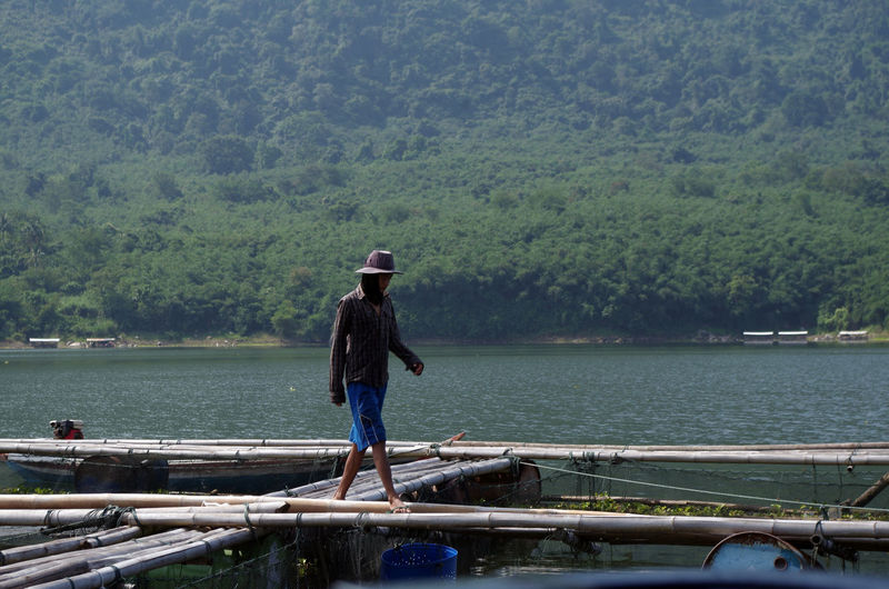 Side view of man walking on bamboos over lake