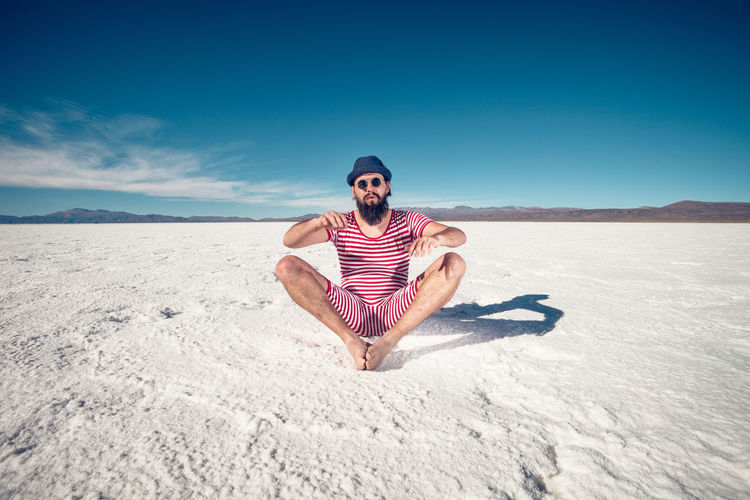 Full length of young man on sand in desert against sky