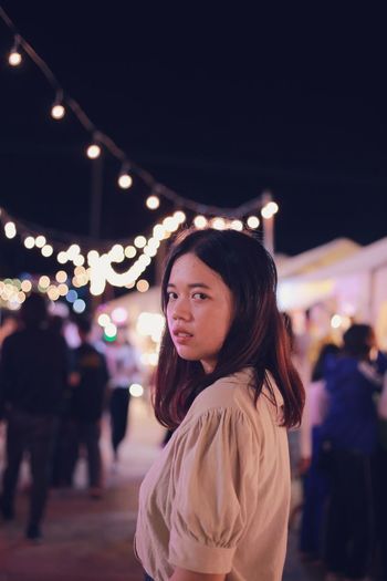 Portrait of young woman standing in illuminated city at night