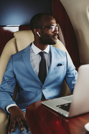 Young businessman looking away with laptop on table in airplane
