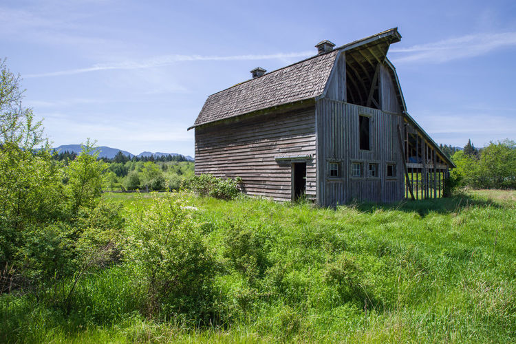 Old wooden barn on grassy field against sky
